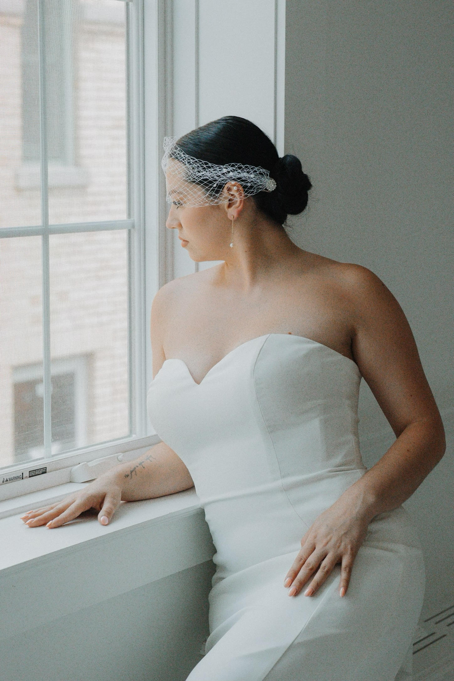 Parella beauty bride looking out window in her gown with beautiful hair and make-up